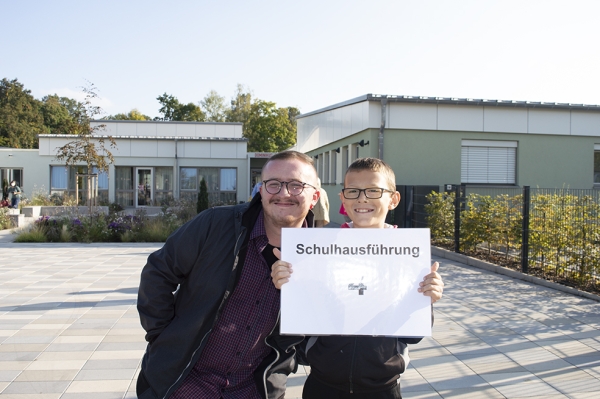 Lehrer und Schüler mit Schild "Schulhausführung"